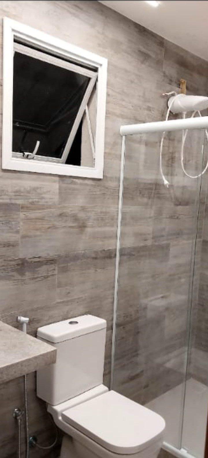Banheiro reformado com revestimento cinza amadeirado, vaso branco e box de vidro